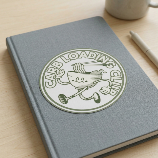 Gray notebook with a 'Carb Loading Club' sticker on a wooden surface