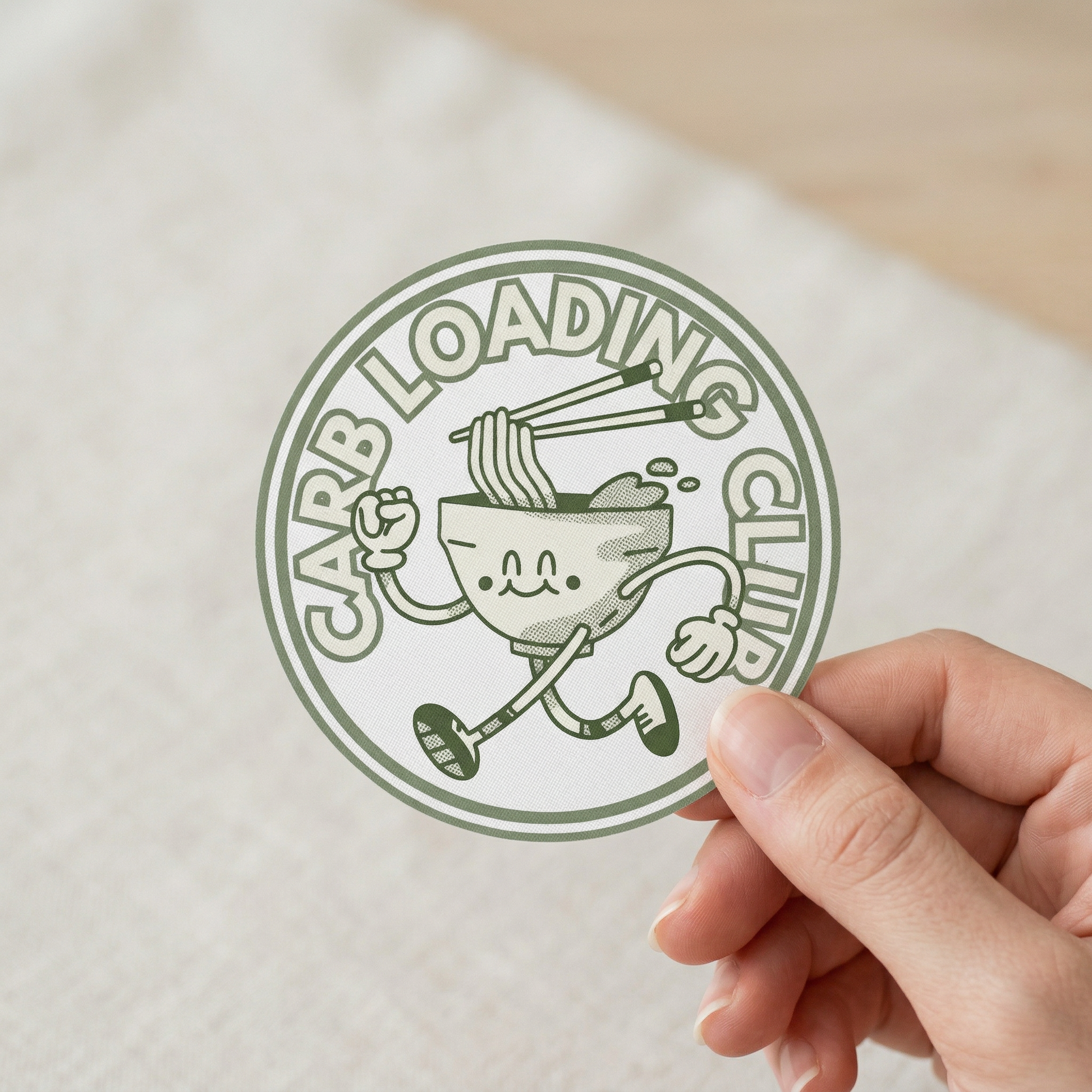 Hand holding a sticker with 'Carb Loading Club' design on a white surface
