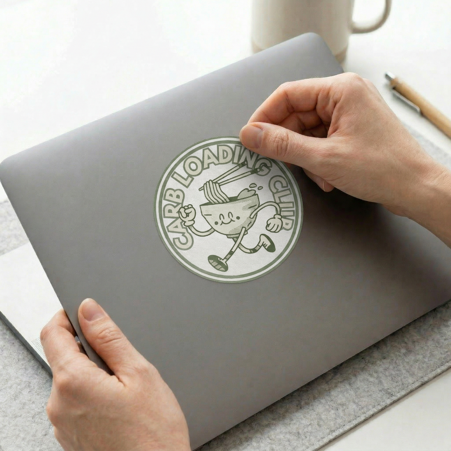Person placing a sticker on a gray laptop with a humorous design.