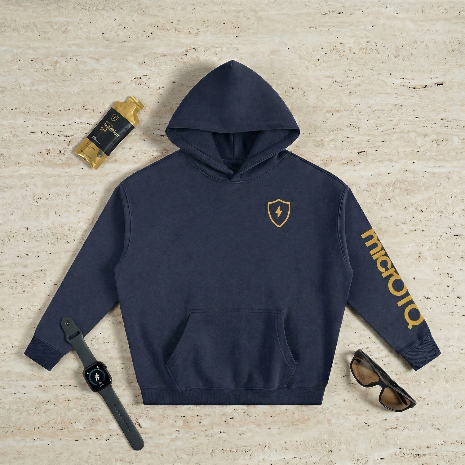 Navy micrOTQ hoodie with The Micro logo on a textured beige surface, surrounded by accessories.