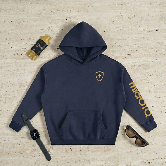 Navy micrOTQ hoodie with The Micro logo on a textured beige surface, surrounded by accessories.
