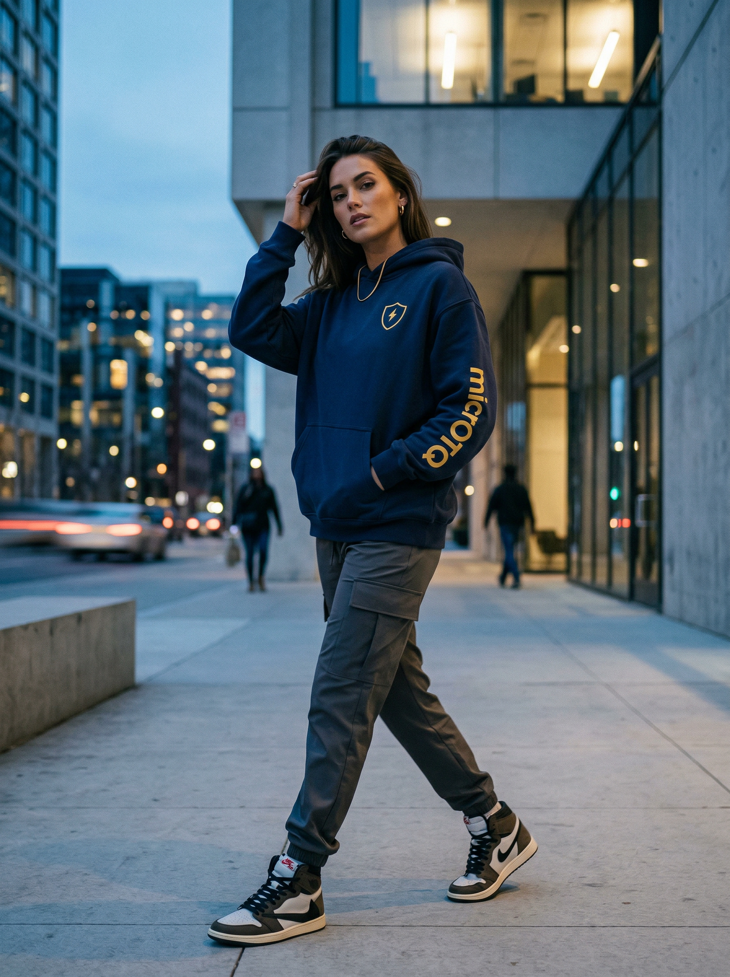 Person wearing a navy hoodie with text, walking on a city street at dusk.