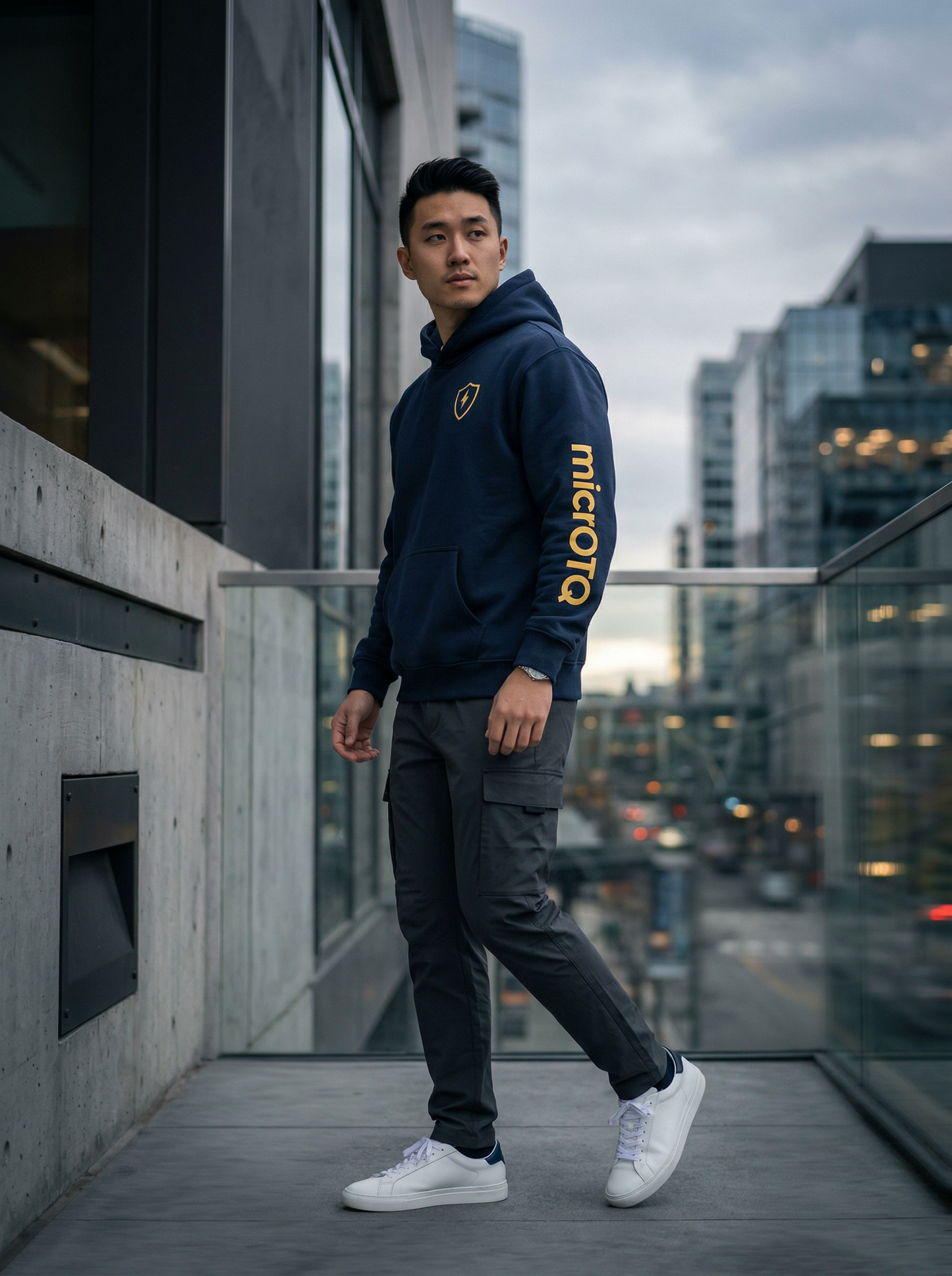 Person wearing a dark hoodie with 'microQ' branding, standing on a rooftop with cityscape background